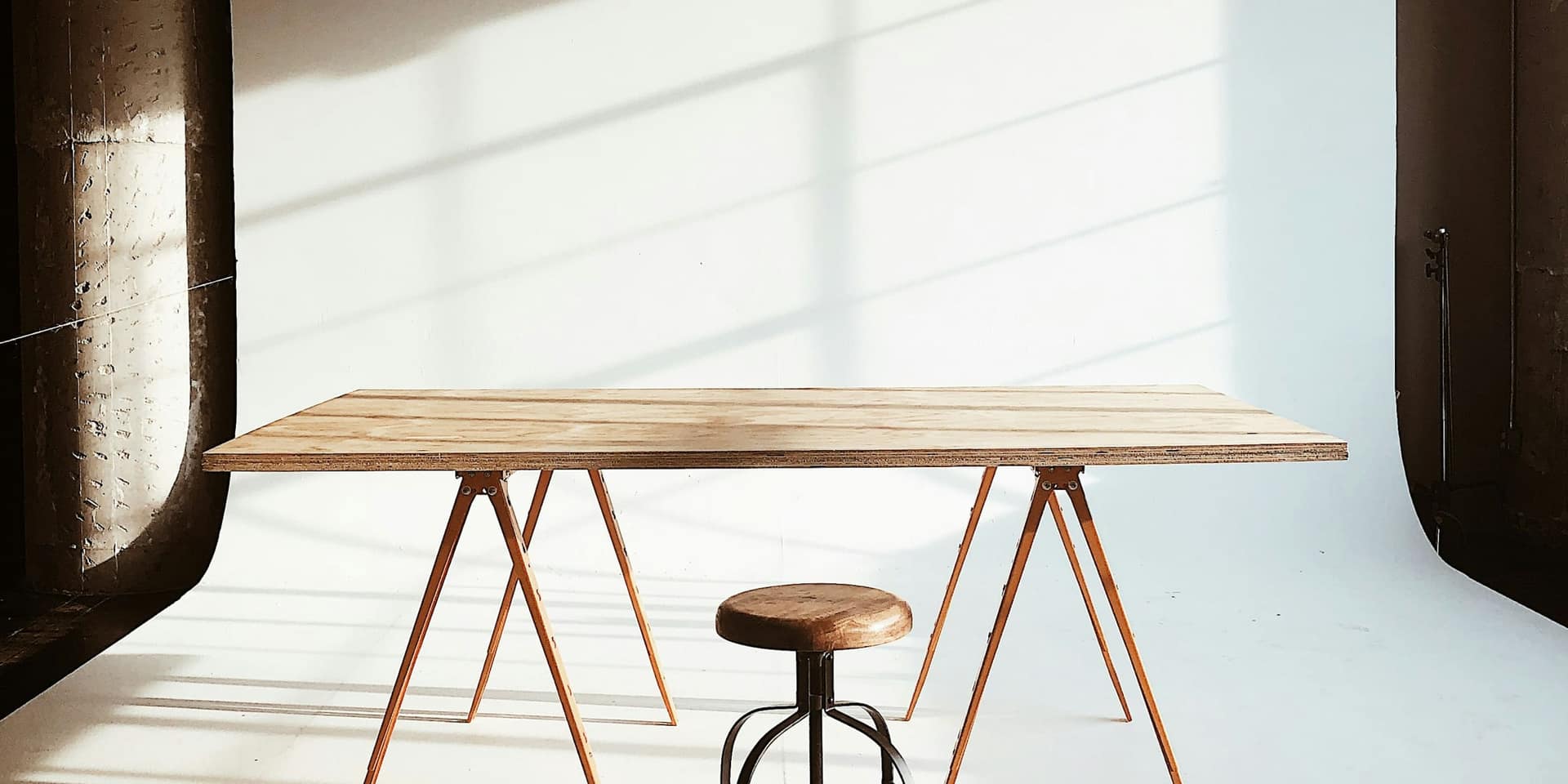 Sunlit studio with a wooden trestle table and a stool