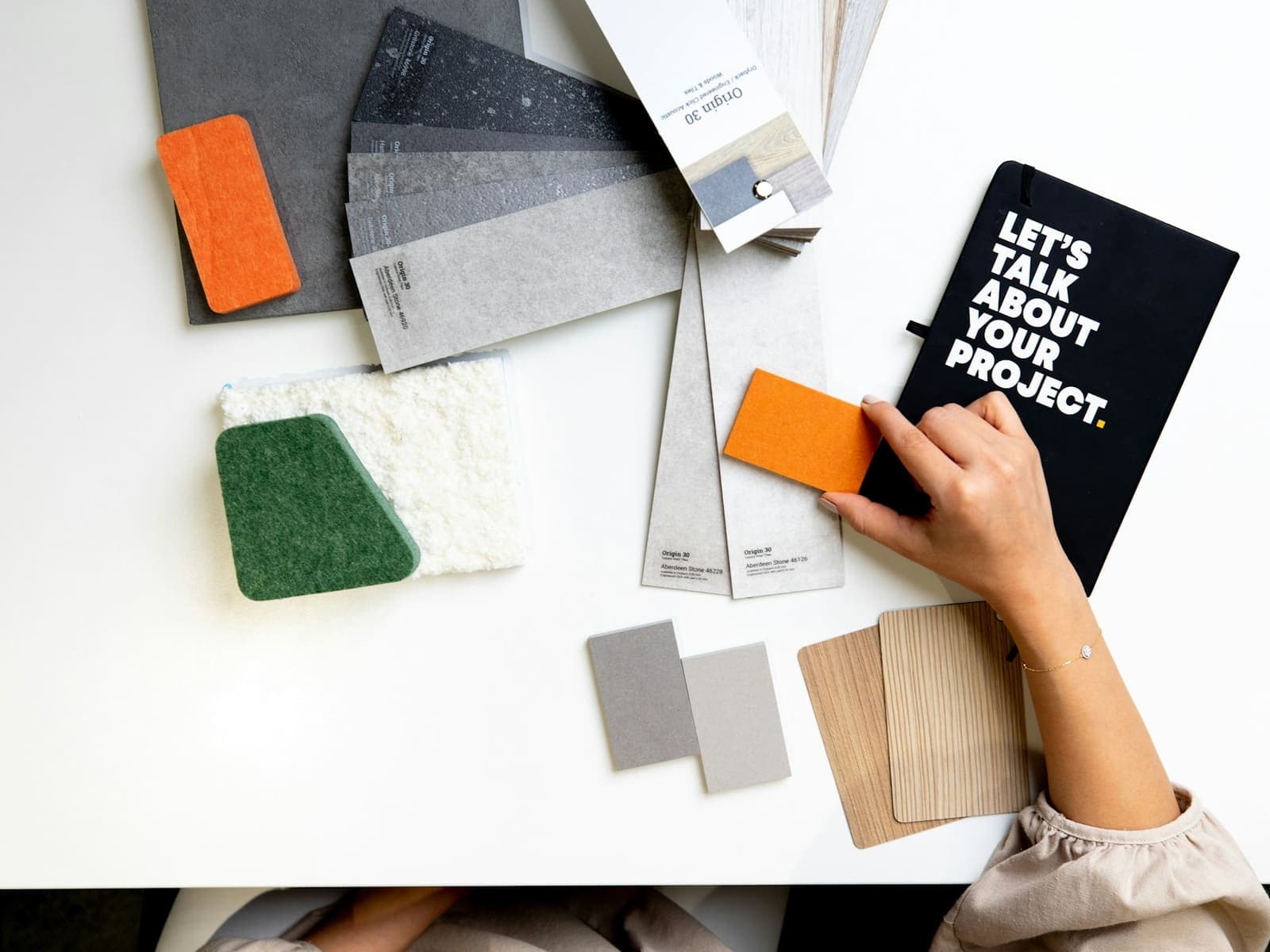 Hand holding an orange material sample over swatches and a notebook