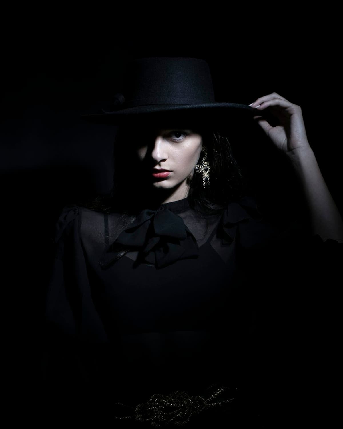 Model in a black shirt and wide-brim hat, lit from the side