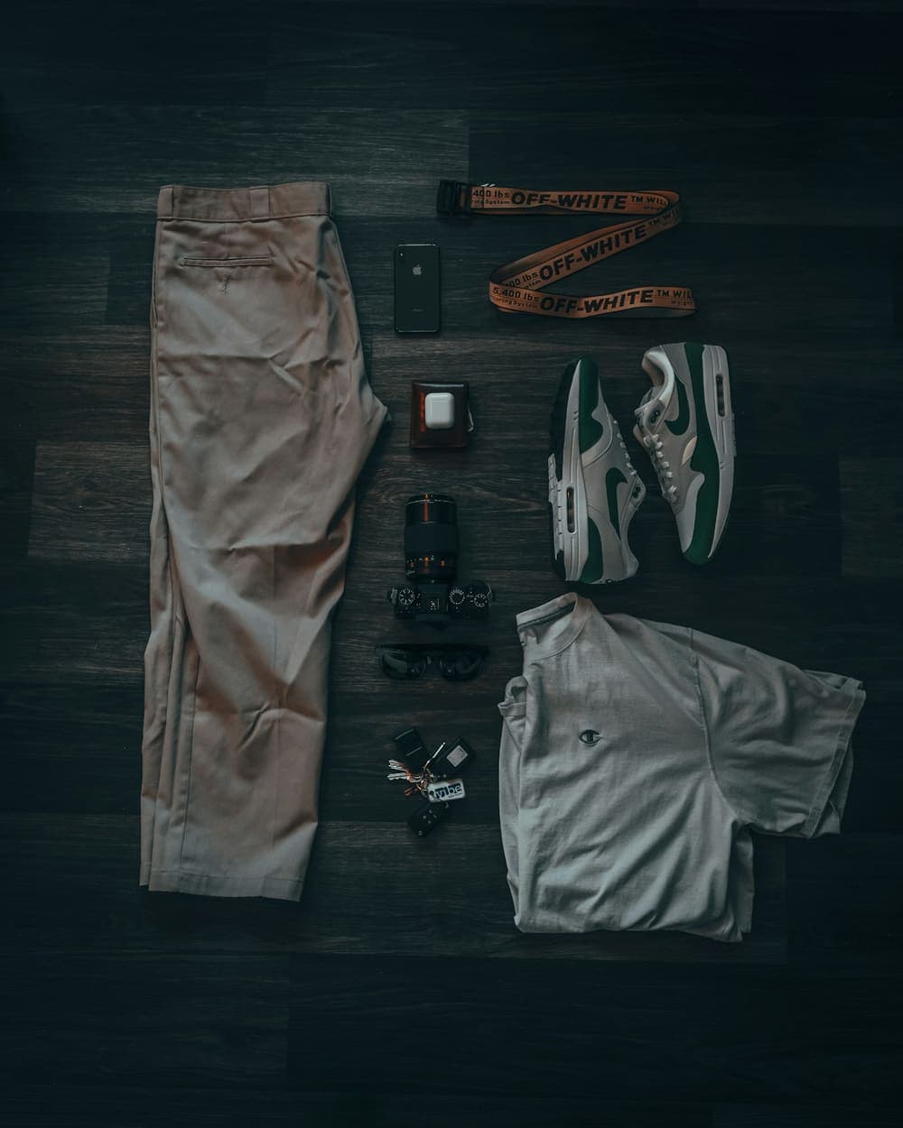 Khaki pants, grey tee and sneakers laid flat on a dark floor